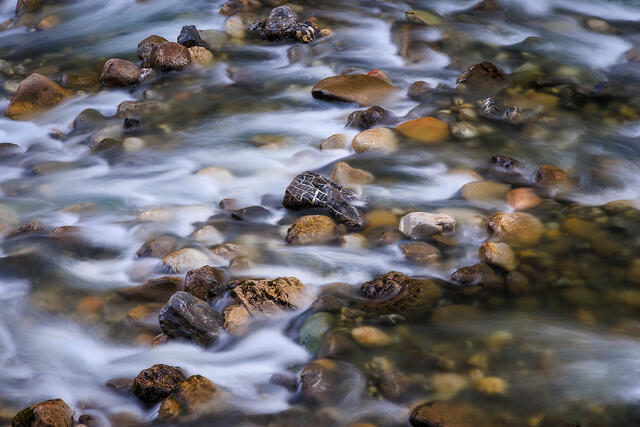 Intimate abstract view looking down at colorful river stones with silky long exposure water flowing over riverbed, Dranse River French Alps France