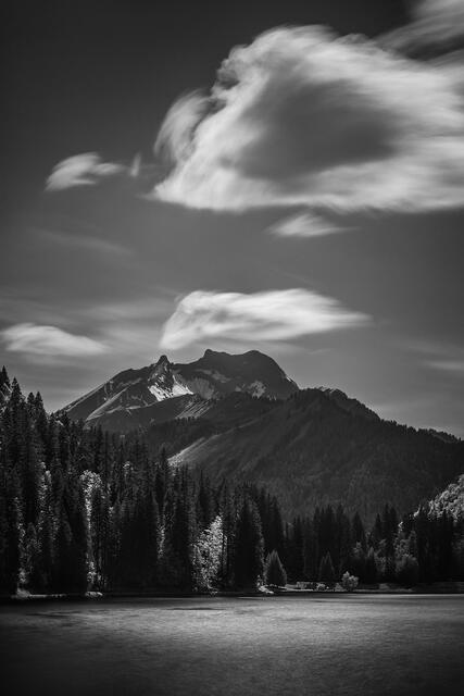 Dramatic black and white long exposure of Alpine mountain peak with streaking clouds over Lake Montriond in the French Alps France