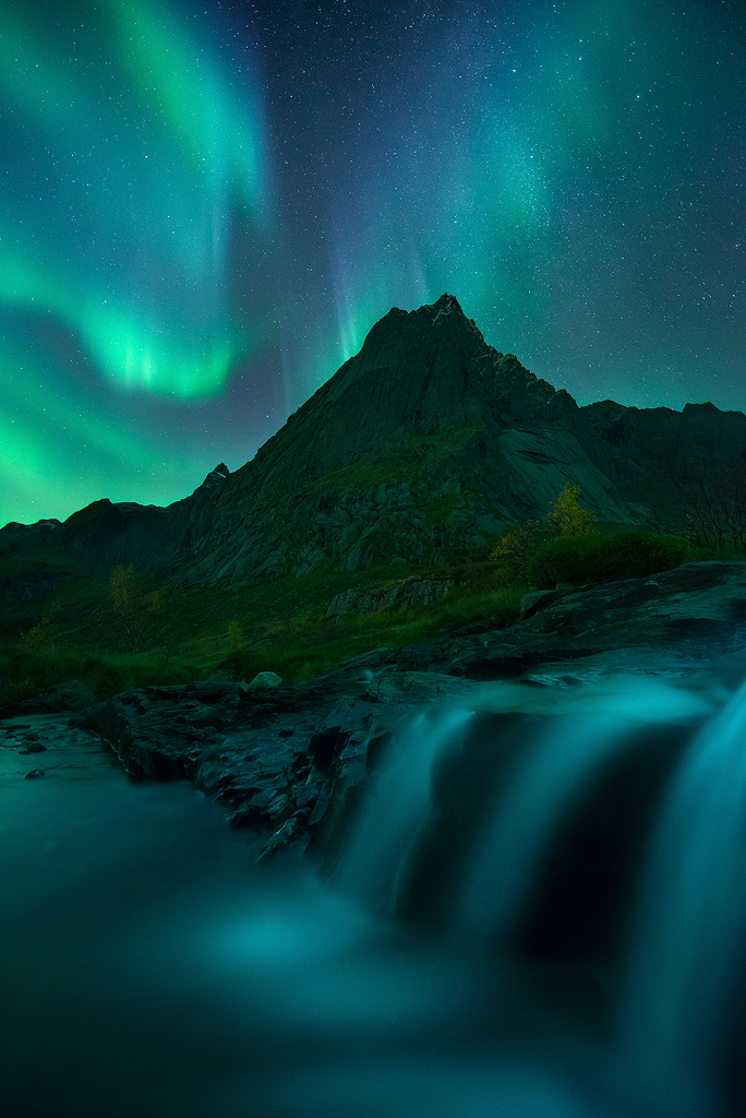 Mountain peak illuminated by aurora borealis above a flowing river in the Lofoten Islands, Norway