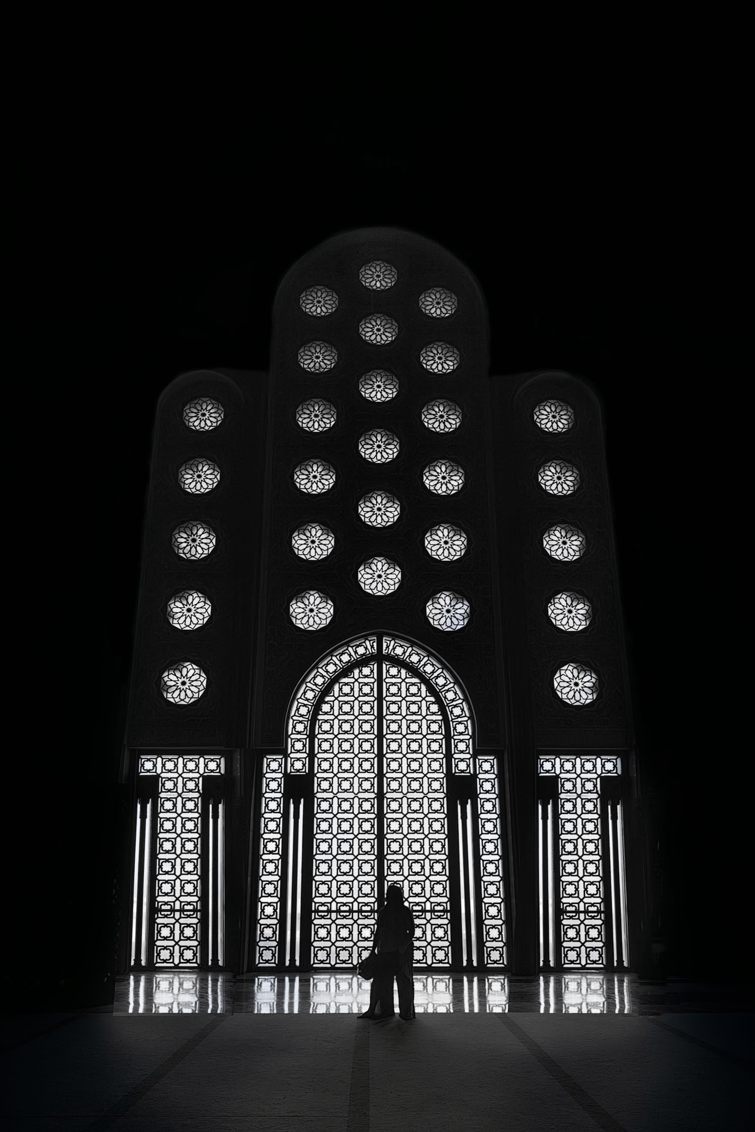 A person stands before the intricate, illuminated designs of the Hassan II Mosque's stunning patterned wall in Casablanca, Morocco.