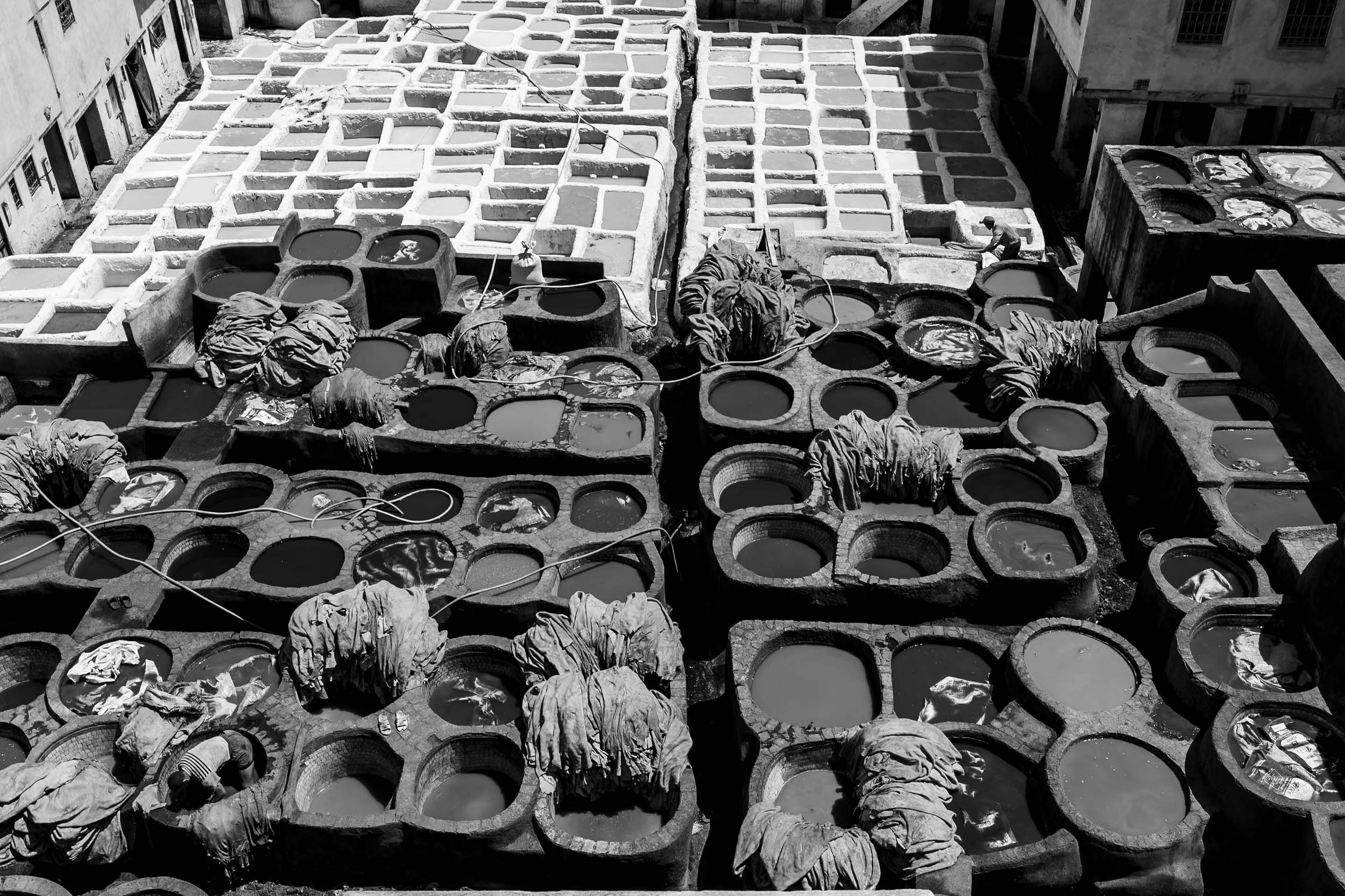 Black and white view of Marrakech dyeing vats, filled with vibrant liquids and cloth pieces, showcasing traditional craftsmanship.