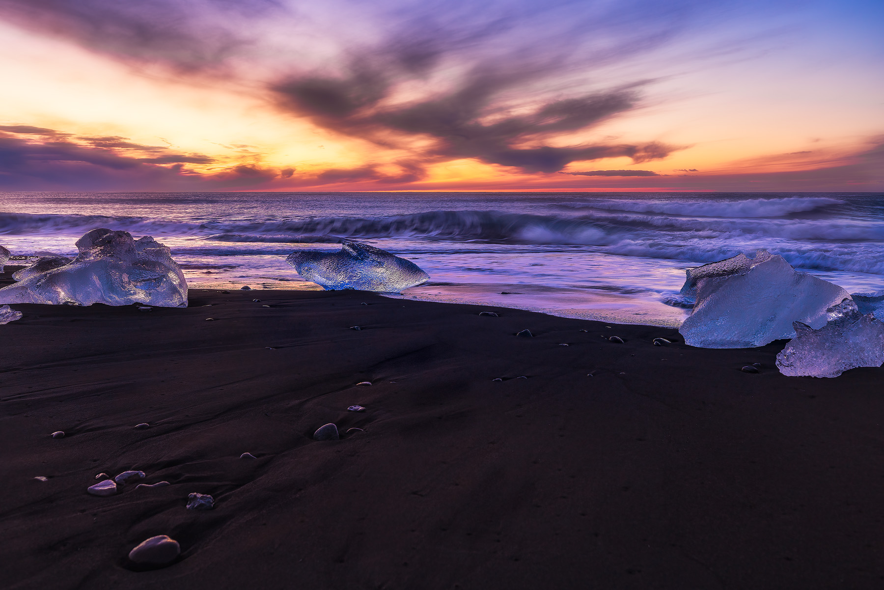 broken chunks of ice on black sand beach at sunrise in Iceland on the south coast.