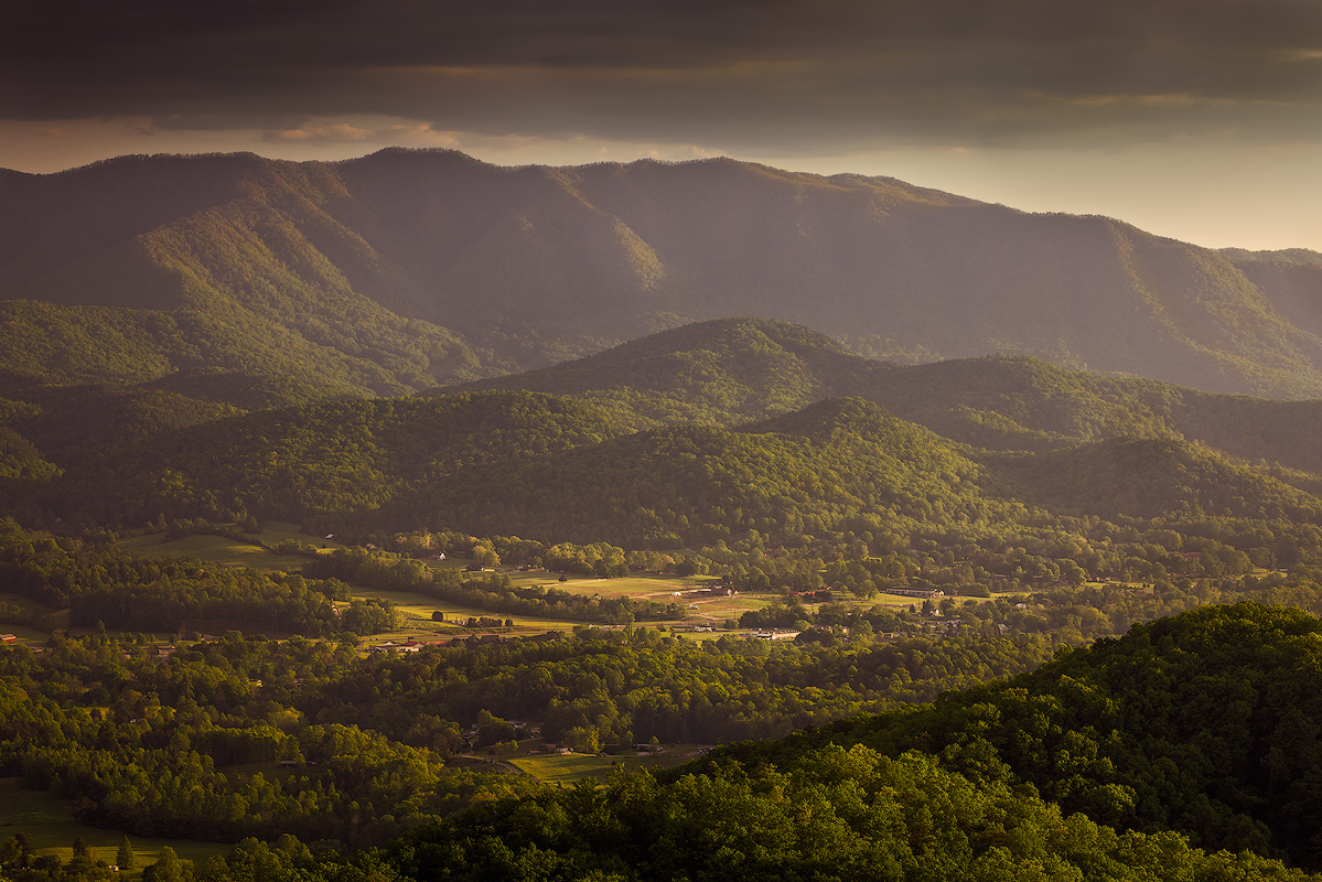 Layered mountain valley landscape sharp from foreground trees to distant ridgeline demonstrating deep depth of field at f/11