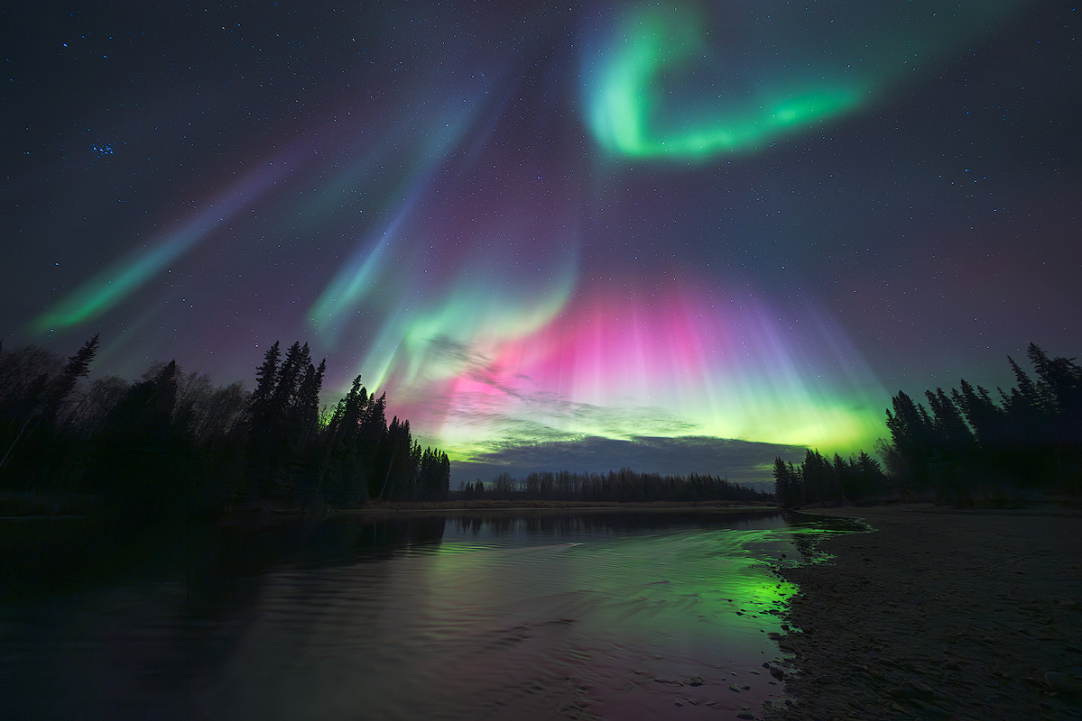 Northern lights with green pink and magenta bands over the Salcha River near Fairbanks Alaska photographed at f/2.8 with aurora reflecting in the water