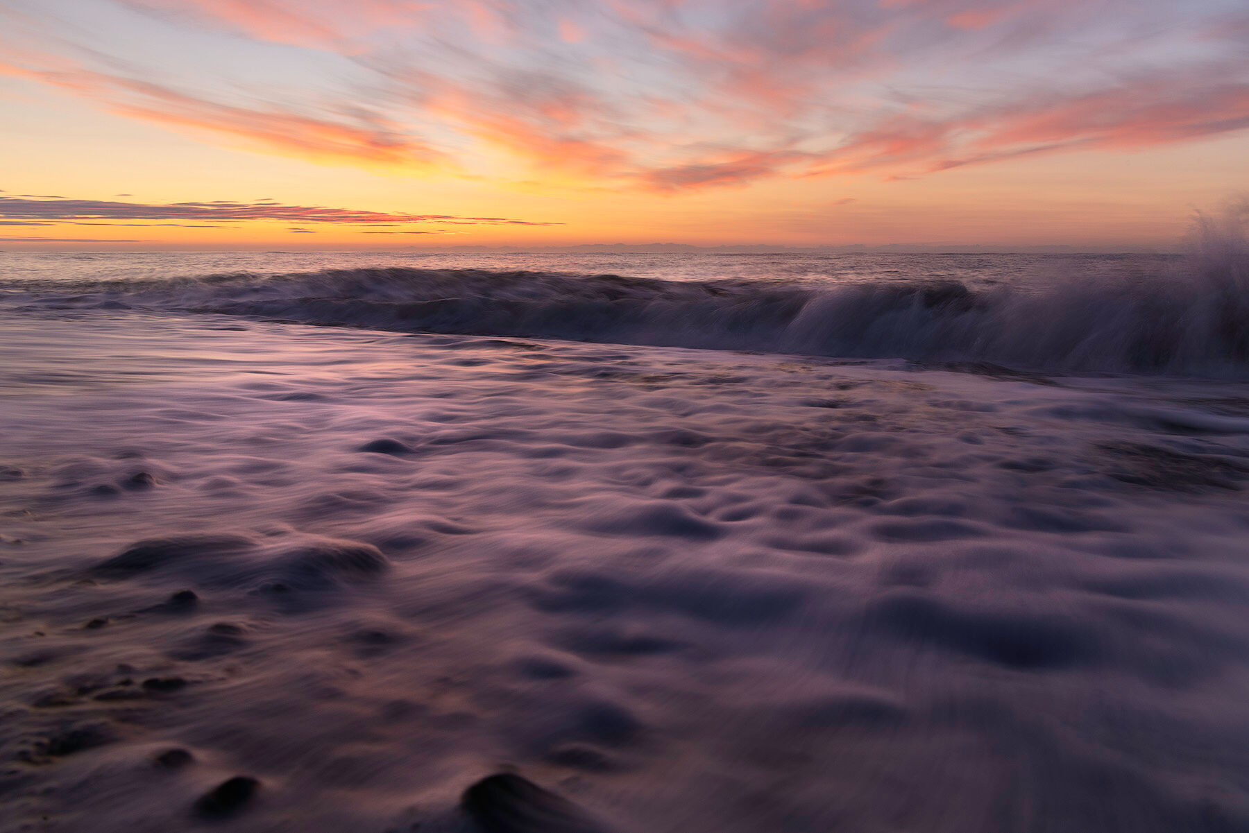 A long exposure of waves washing over a pebble beach on Cook Inlet at Silver Salmon Creek in Lake Clark National Park, under streaks of pink and orange cloud.