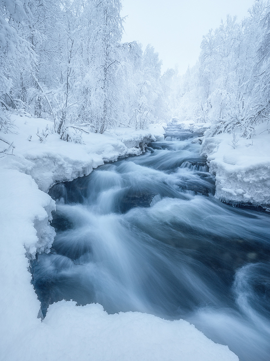 Frozen waterfall and winter stream in a snow-covered Northern Norway forest