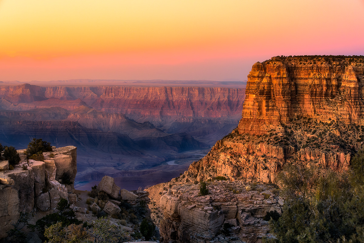 Golden Hour Spectacular sunset over Grand Canyon National Park with golden light illuminating layered canyon walls beneath vibrant pink and orange gradient sky in Arizona