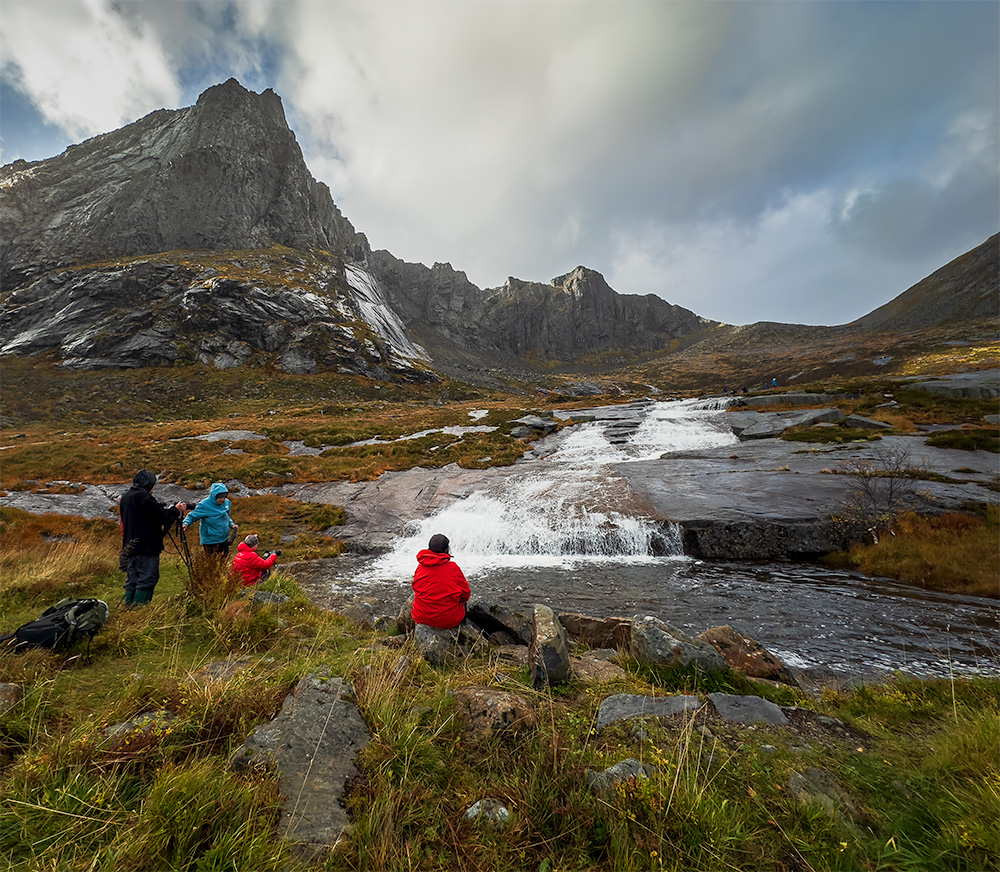 Photographers photograph the landscape of Norway, cascading water with mountains in background under moody clouds
