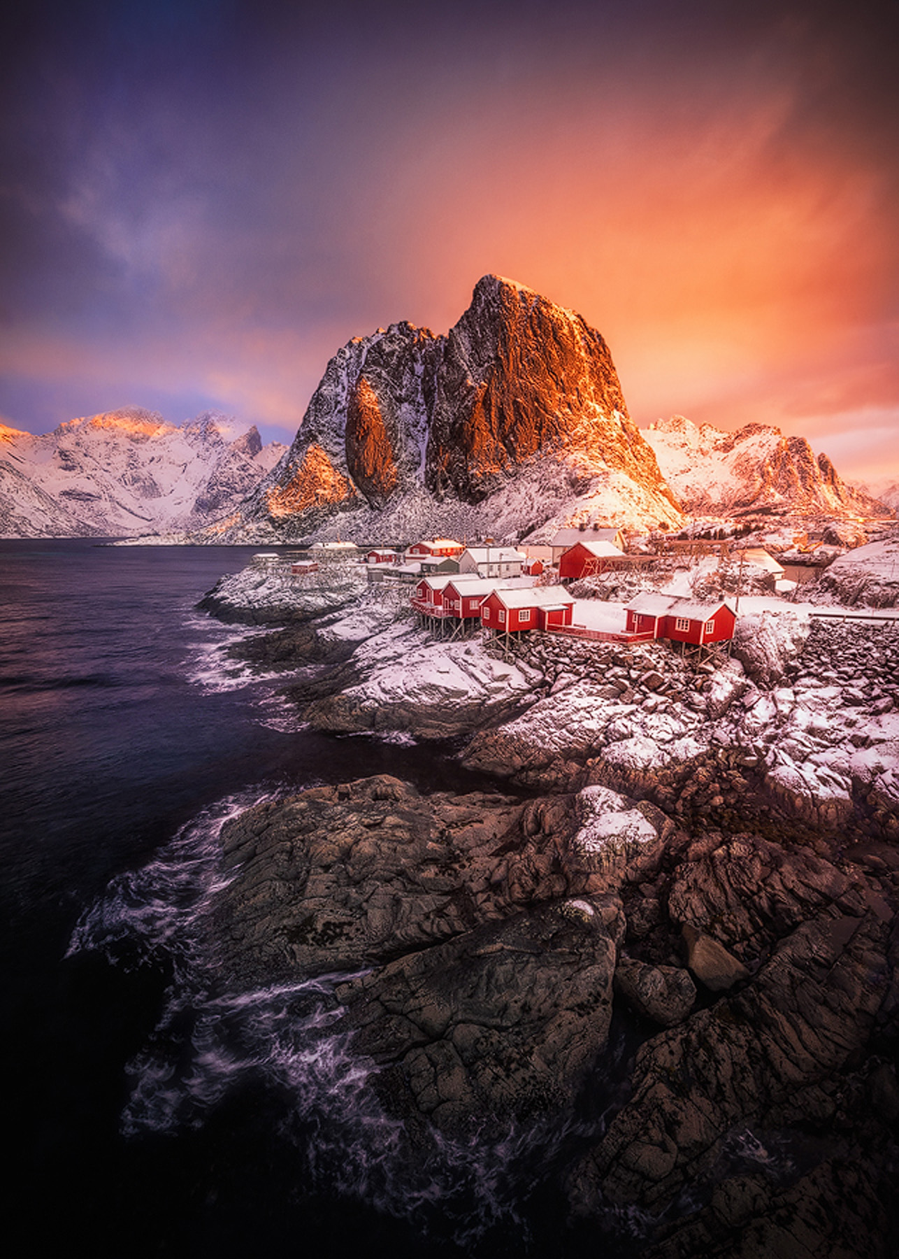 Pink sunrise over snow-covered peaks and the rorbuer cabins at Hamn&oslash;y in Lofoten in winter