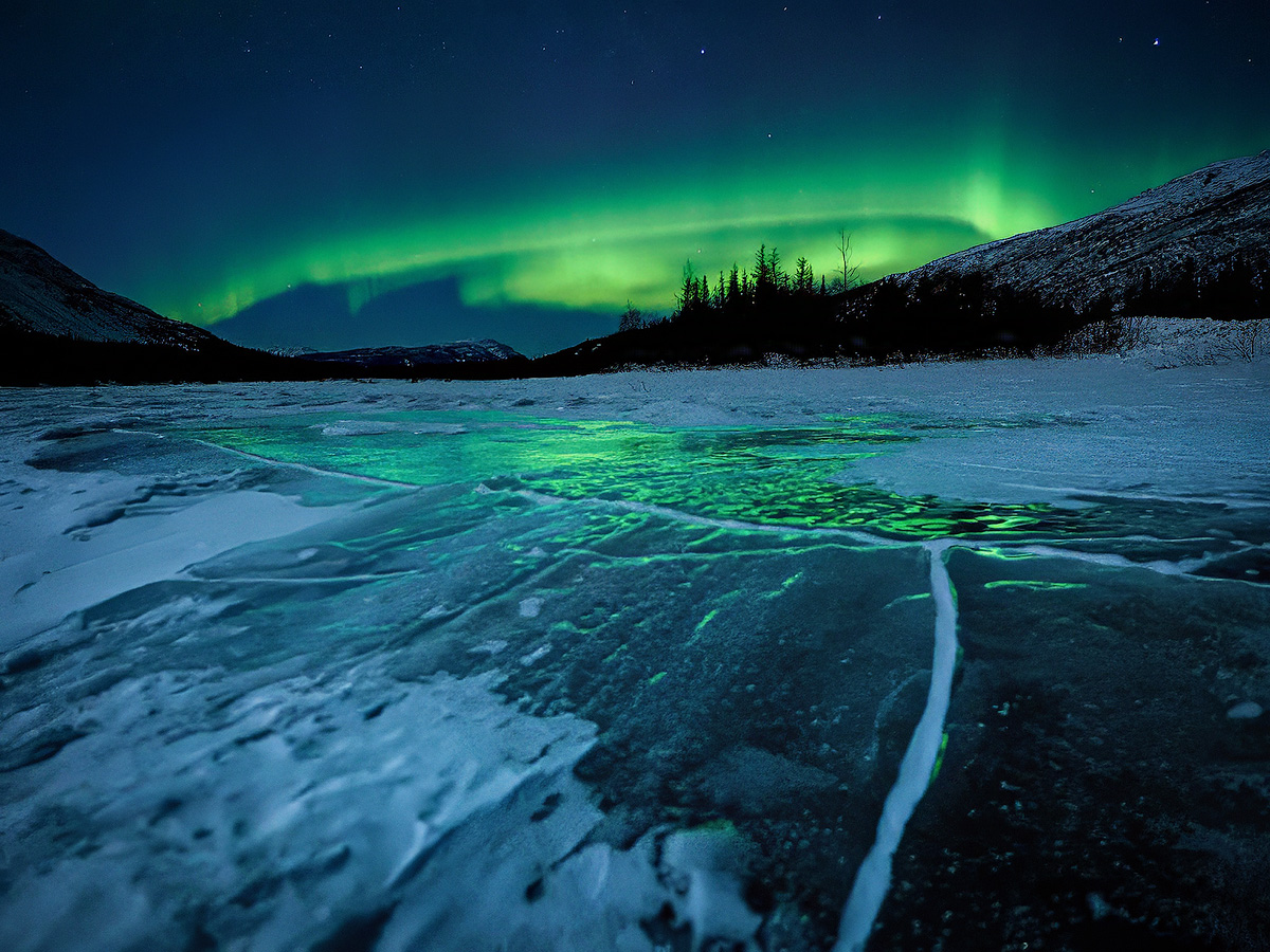 Aurora arc reflected in cracked river ice with mountains and boreal forest during the Spring 2026 Northern Lights Workshop in Alaska