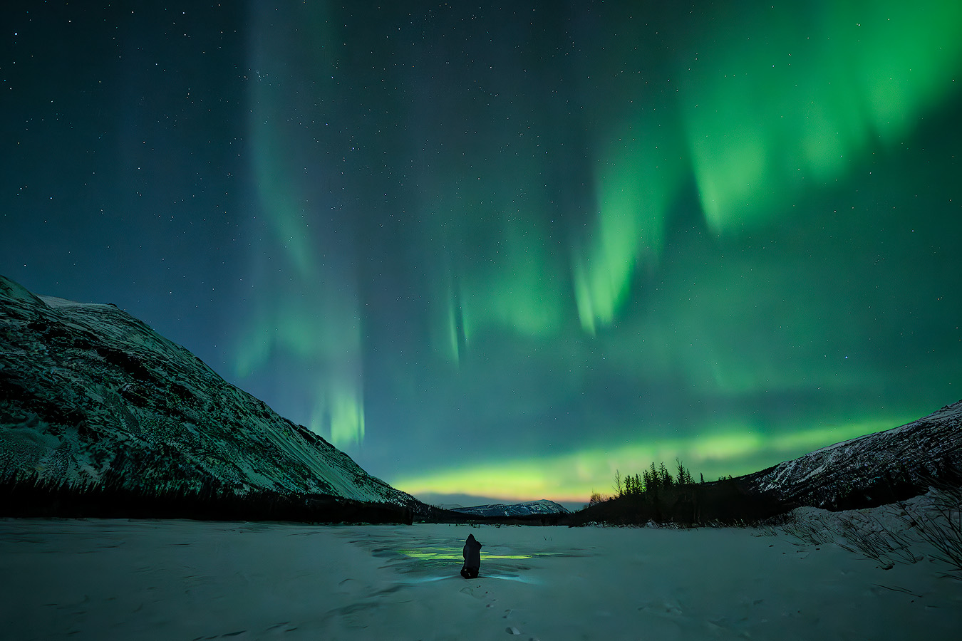 Michael Schultz photographing aurora curtains over a frozen river with mountains framing the scene during the Spring 2026 Northern Lights Workshop in Alaska