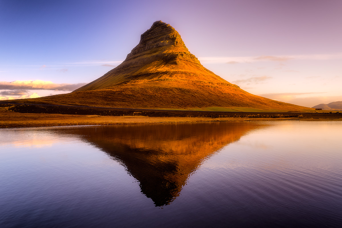 Kirkjufell mountain glowing amber in golden hour light with near-perfect reflection in still water creating symmetrical diamond composition in Iceland