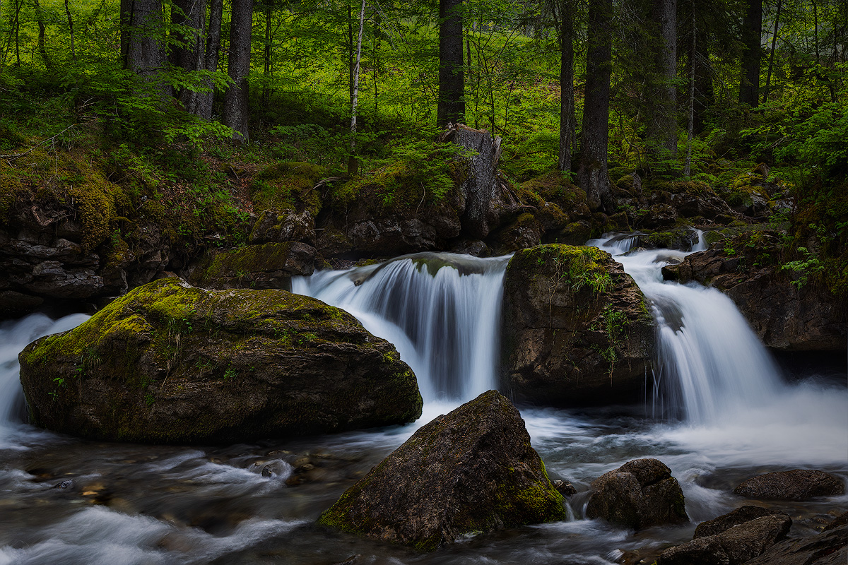 Forest waterfall cascading over mossy boulders at Cascade d'Ardent France with sharp detail throughout the frame shot at f/11