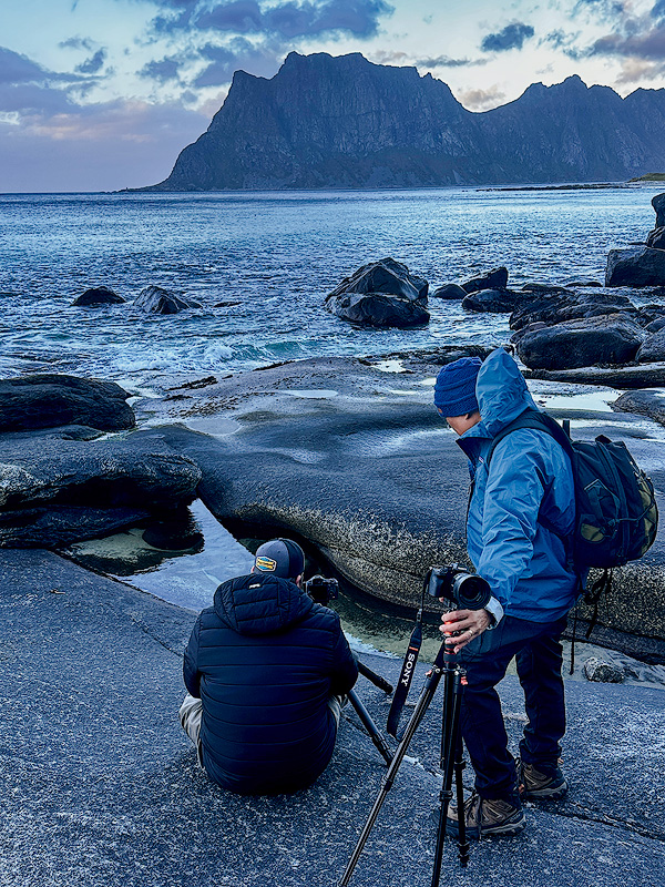 Michael Schultz teaching focus stacking technique to workshop participant on rocky Norwegian coastline during Face The Outdoors Photography landscape workshop