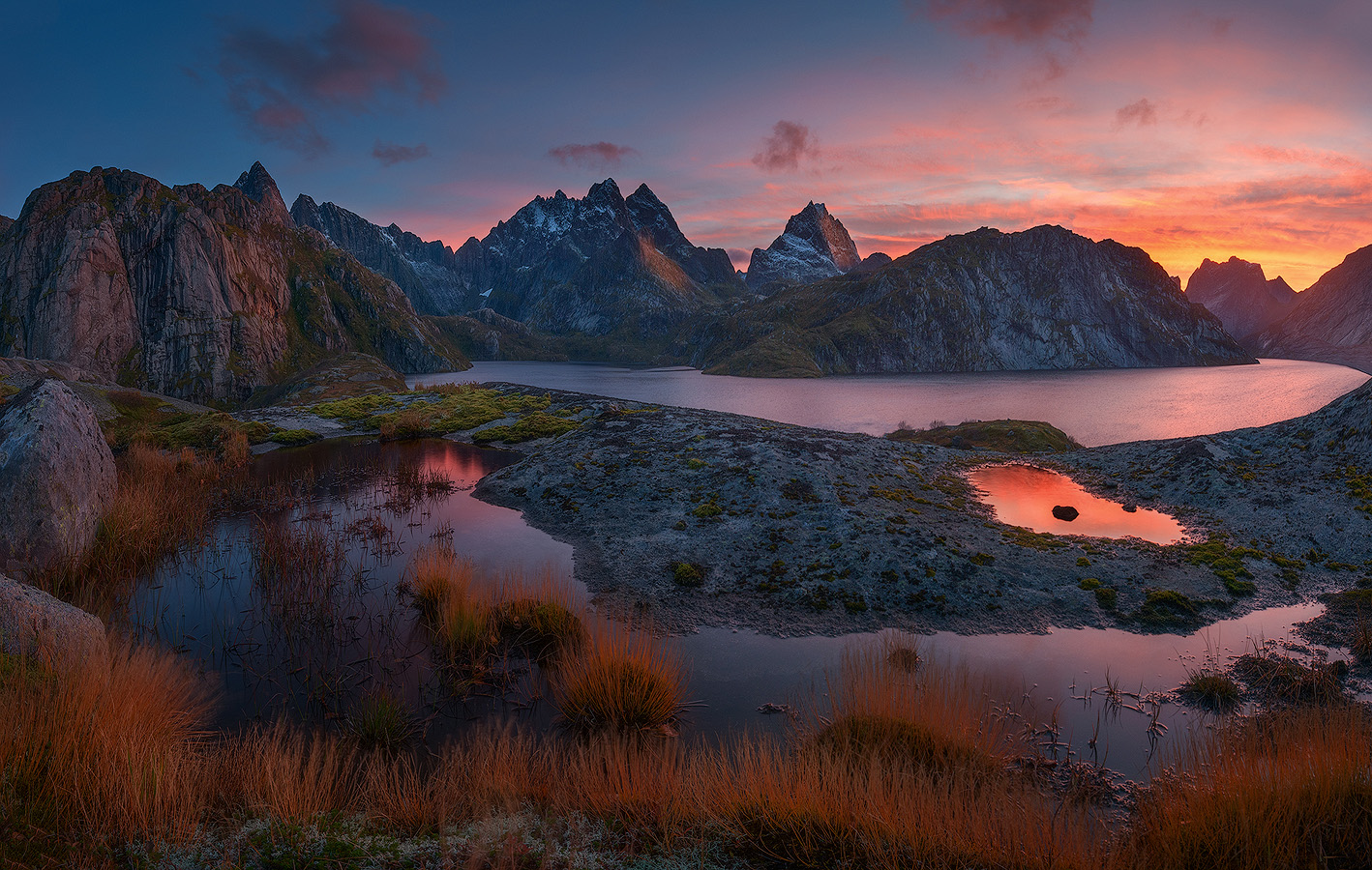 Lofoten Islands alpine tarns reflecting pink sunset light with jagged granite peaks silhouetted against the Arctic sky in Northern Norway