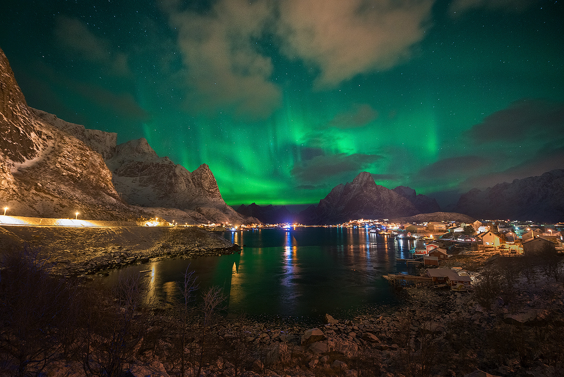Northern lights over a Lofoten harbor village and mountains on a winter night during a photography workshop