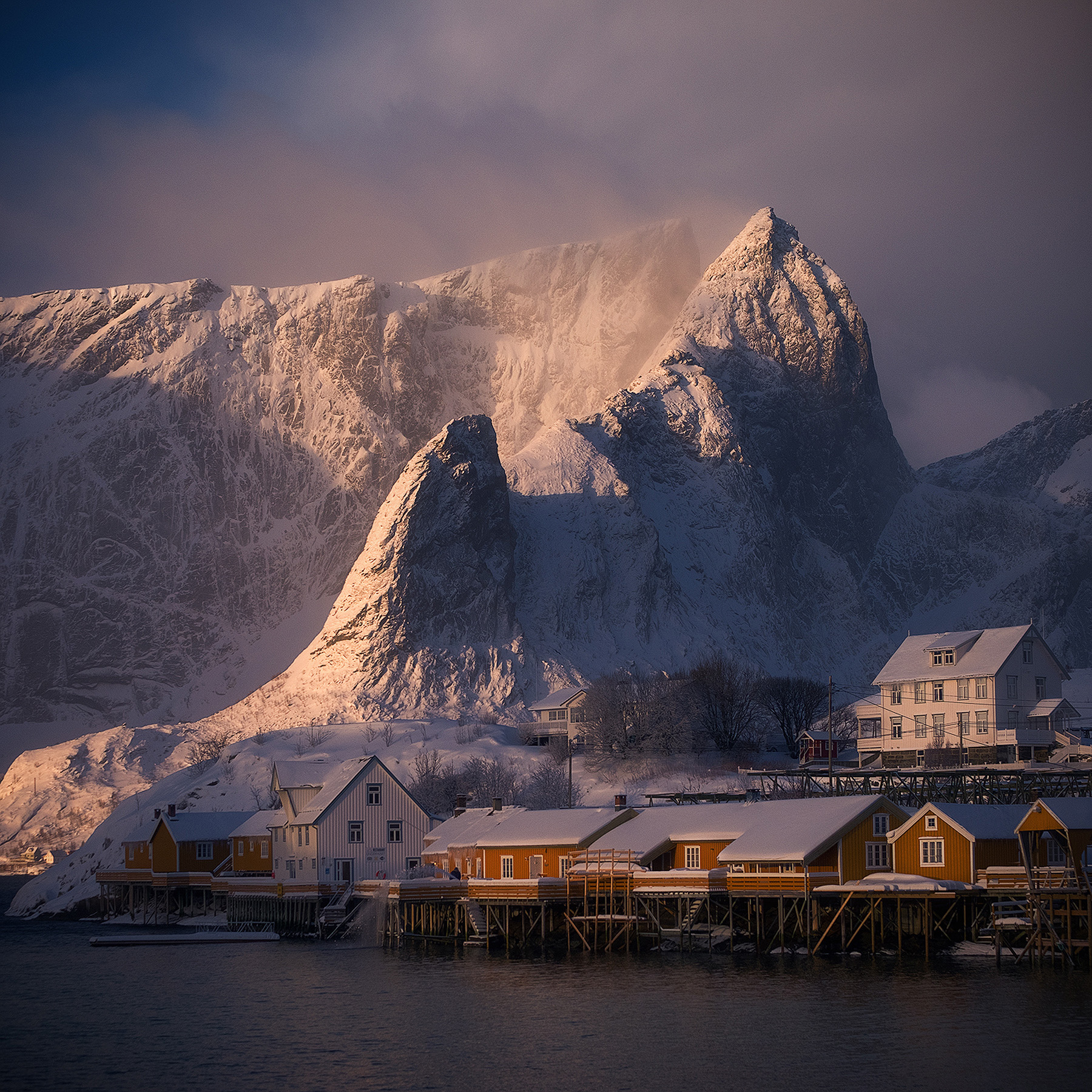 Snow-covered peaks lit by low winter sun above houses in a Lofoten village, on the route of the Lofoten winter photography workshop