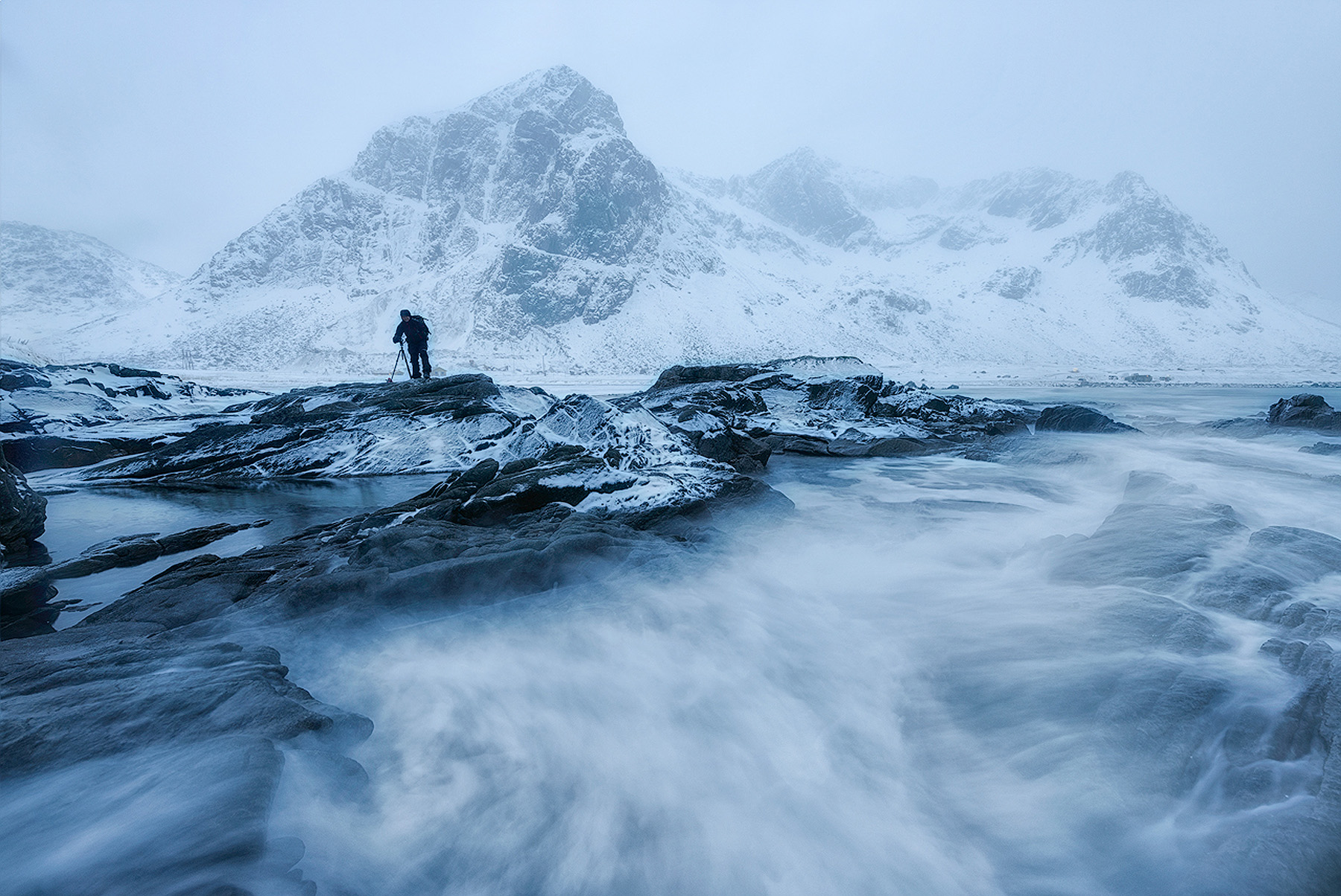 Photographer standing on snowy rocks in a winter snowstorm on the Lofoten coast during a winter photography workshop in Norway