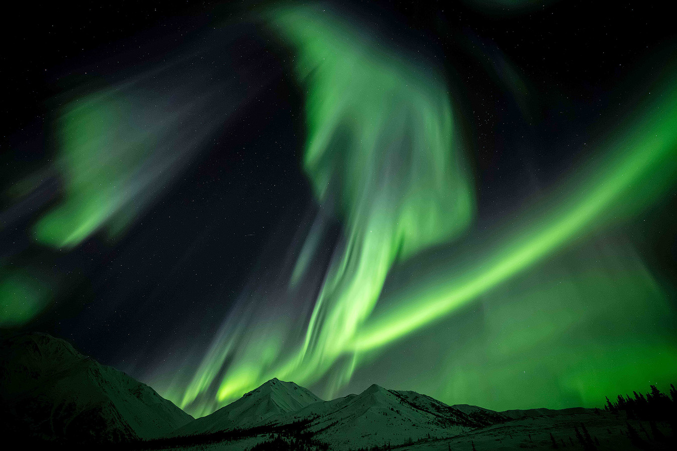Active aurora substorm with green vertical curtains over snow-covered ridges during Workshop Two of the Spring 2026 Northern Lights Workshop in Alaska