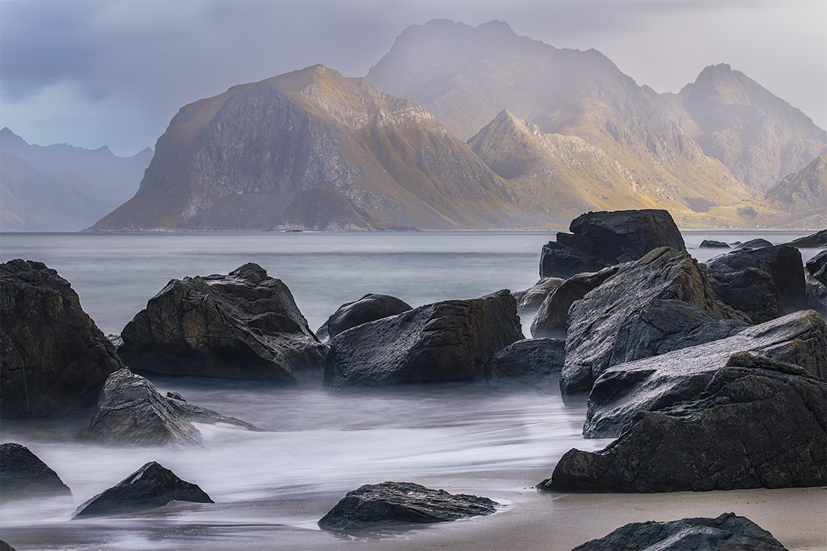 Warm glow from the sunset lights the mountains in the background with a rocky beach in foreground