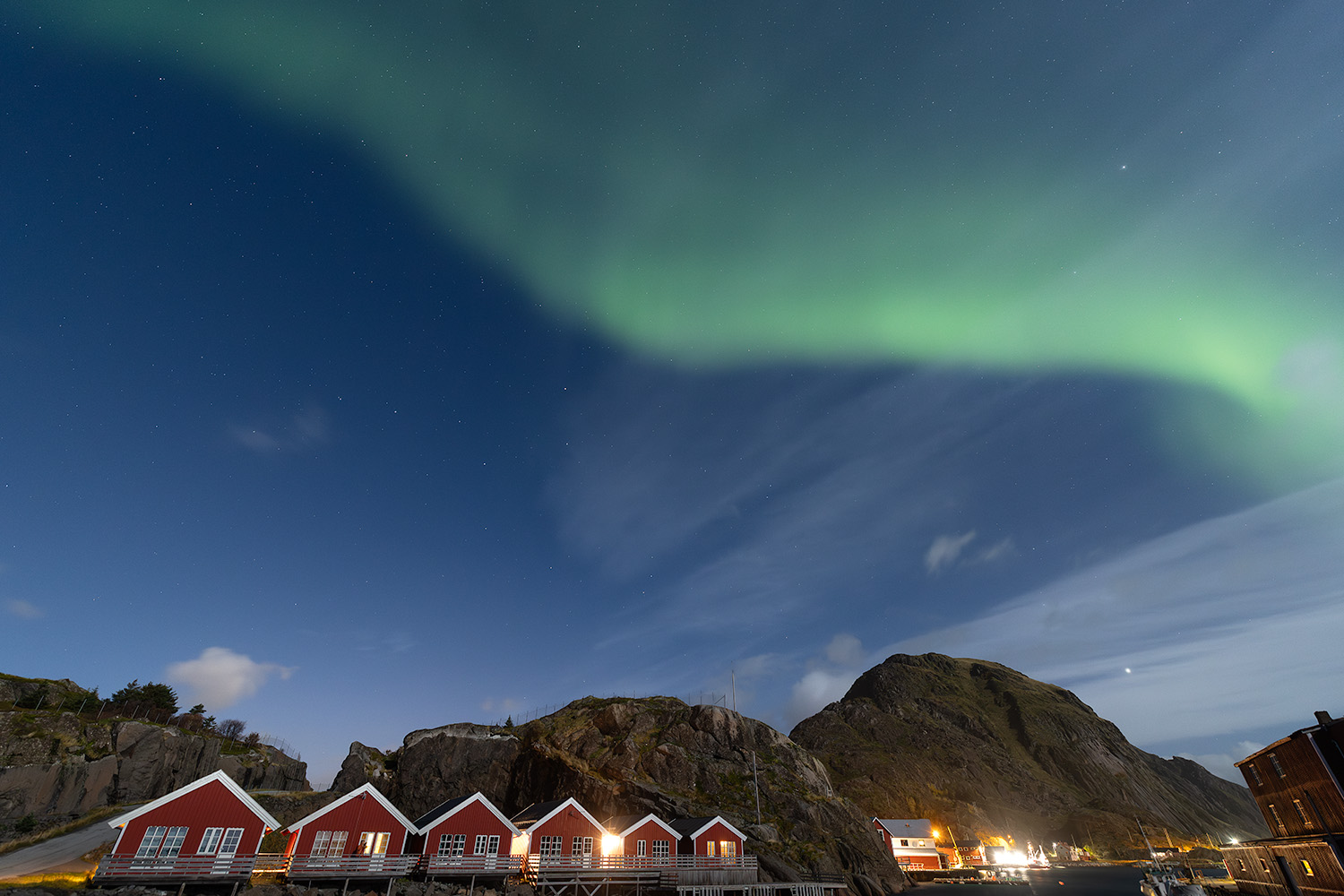 Northern lights dance over red fisherman cabins in Lofoten Islands, Norway