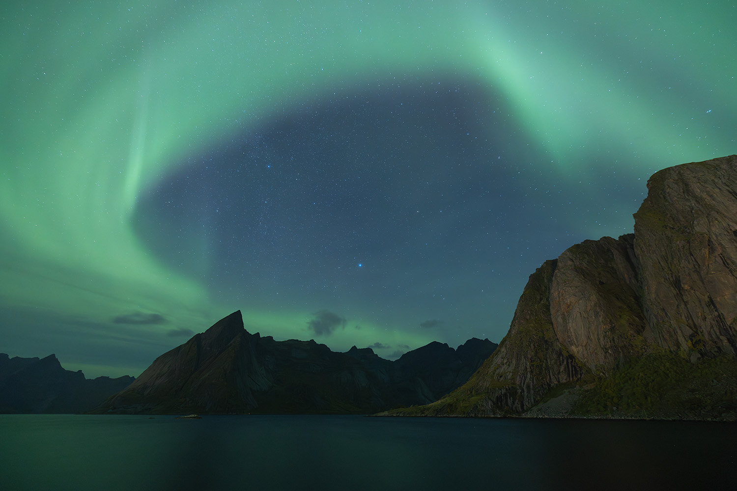 A vibrant display of northern lights dance over jagged mountains reflecting in the open water