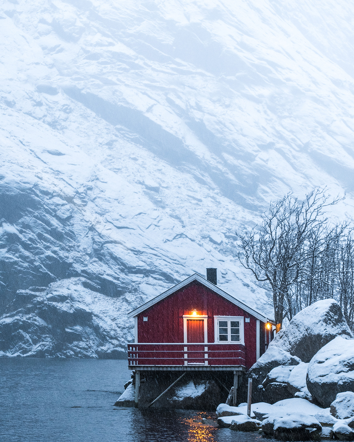 Red house in the snow below a steep snow-covered mountain at Nusfjord in Lofoten