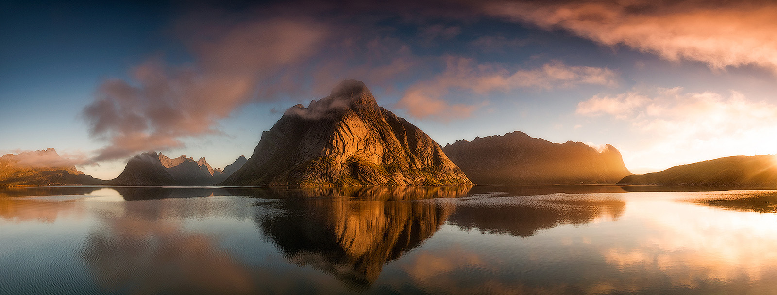 Olstind mountain reflecting in calm Reinefjord waters at sunset, Lofoten Islands, Norway