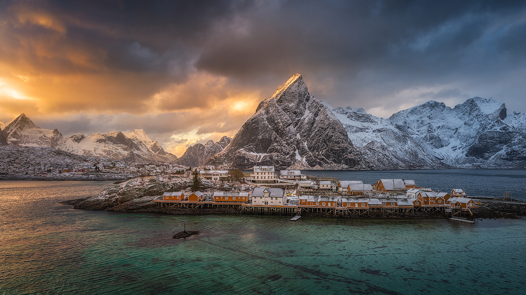 Golden sunrise over snow-covered Olstind and the yellow rorbuer of Sakris&oslash;y in Lofoten in winter