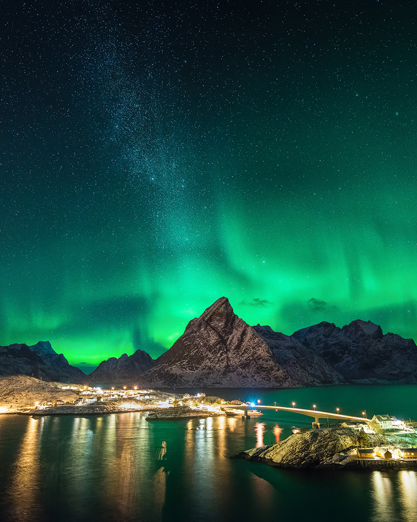 Green northern lights and the Milky Way over Olstind and the lights of Sakris&oslash;y village in Lofoten