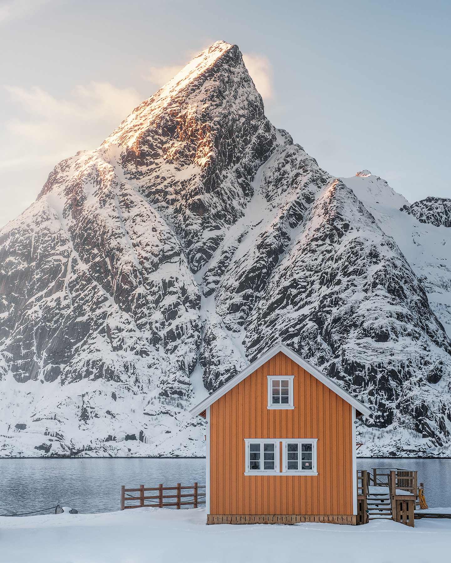 Orange fishermen's cabin at Sakris&oslash;y below the snow-covered peak of Olstind in Lofoten winter light