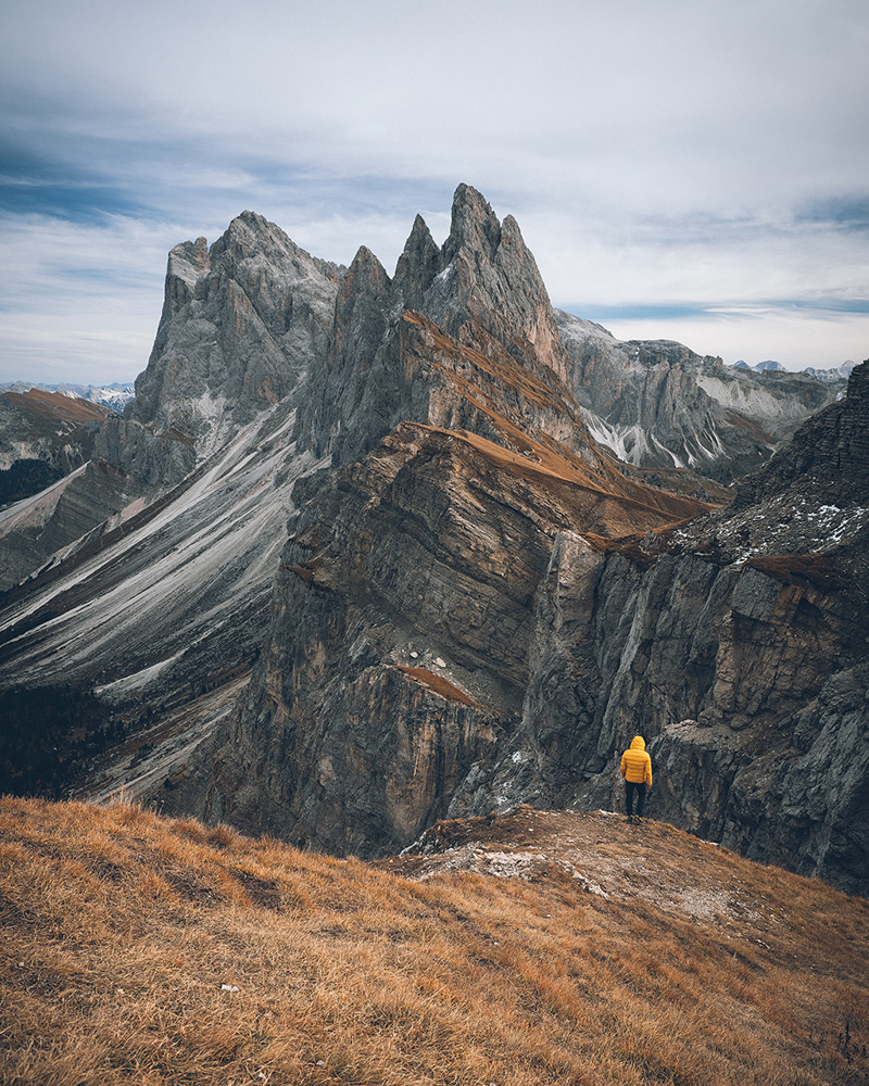 Hiker on Seceda ridgeline in Italian Dolomites with dramatic peaks and autumn grasslands October photography