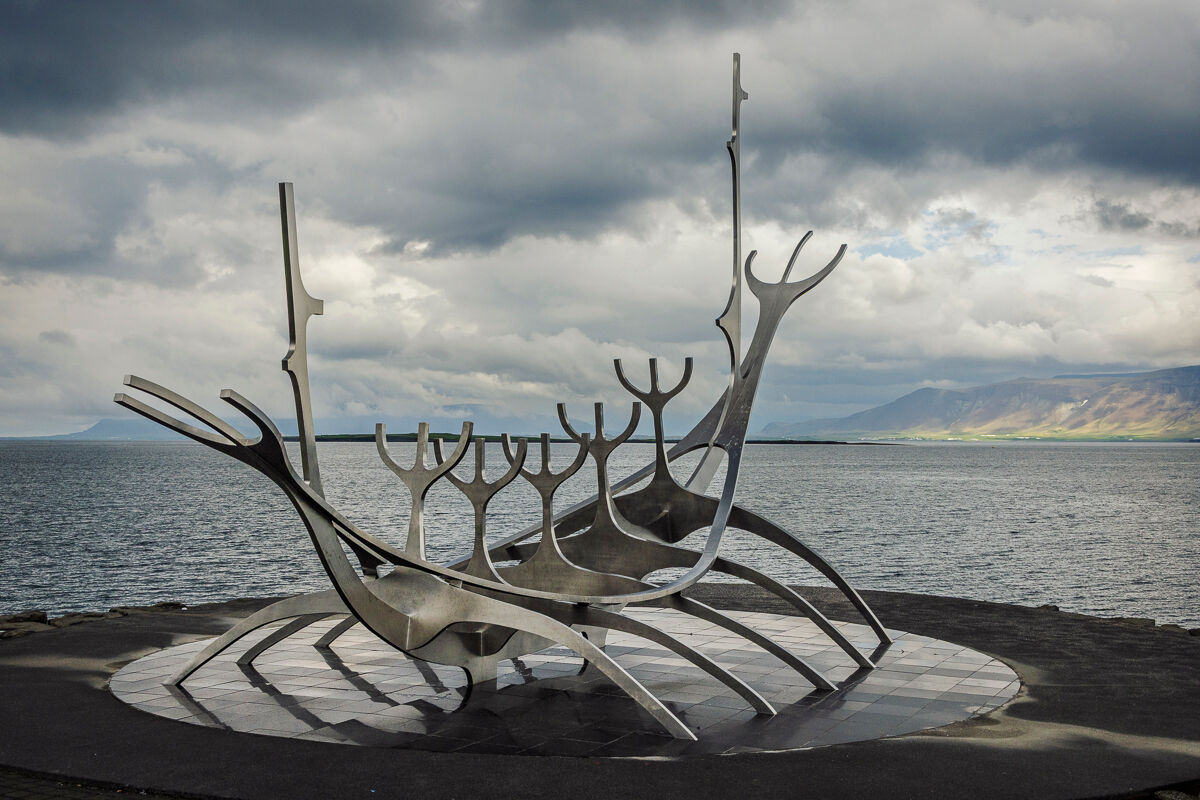 A metallic sculpture resembling a Viking ship, overlooking a calm sea with cloudy skies.